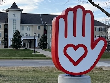 A large red and white hand statue with a heart in front of a building