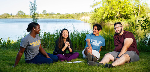 Four people sitting on the grass in a semi-circle, talking and laughing