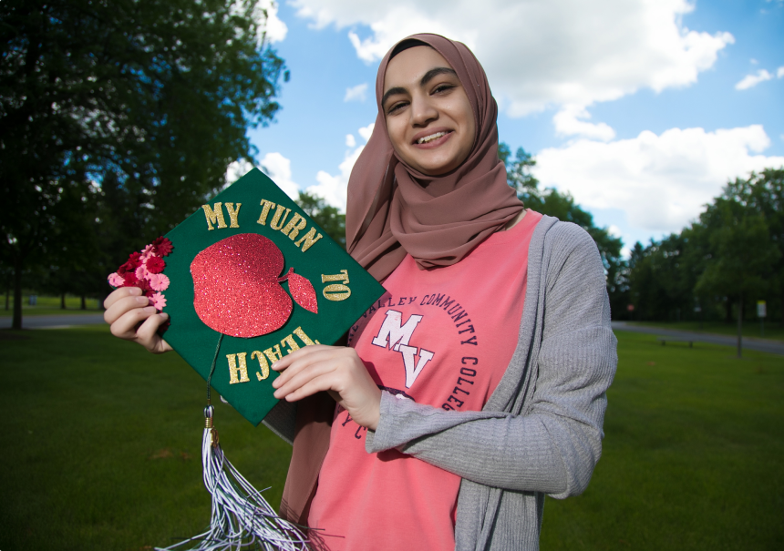 Rama Diab, graduate of GovState, holding a graduation cap that says, ‘my turn to teach’