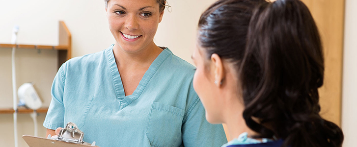 Clinical medical assistant smiling at patient while holding clipboard