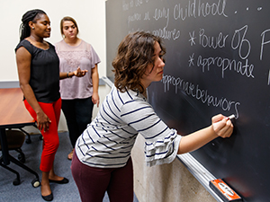 Student writing on chalkboard while other students watch Student writing on chalkboard while other students watch