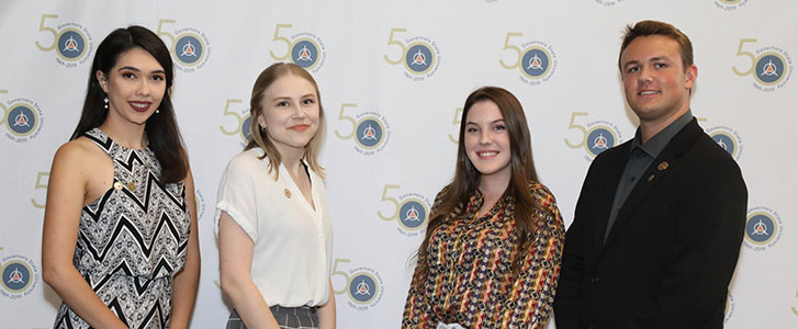 Students smiling in front of Governors State University 50th Anniversary logo backdrop