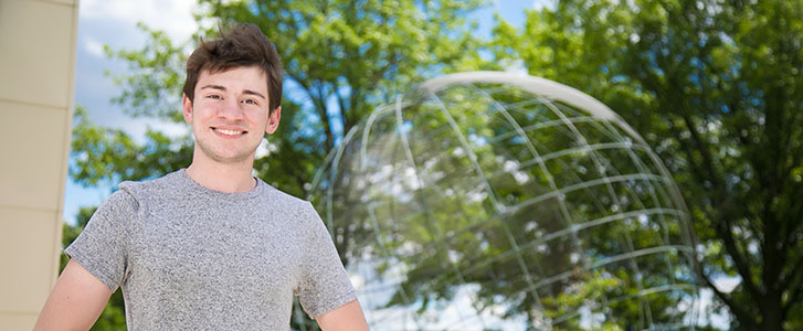 Student smiling outside next to globe statue