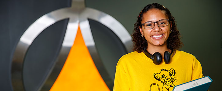 Student smiling while holding book in the library–in front of Governors State logo