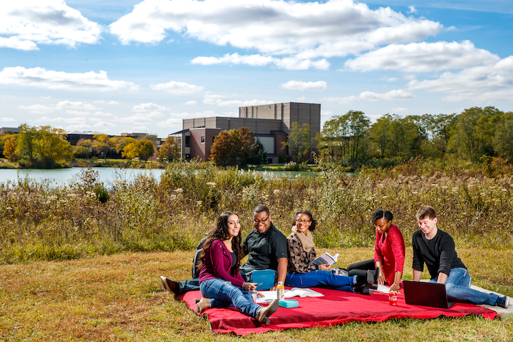 Students sitting on blanket outside of campus by pond
