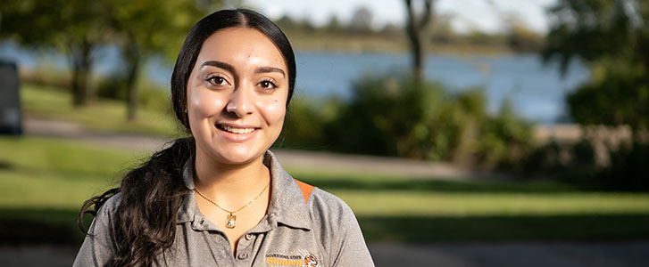 Student ambassador smiling outside the university cafeteria near the pond.