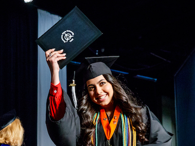 Graduate holding up degree on stage during Commencement ceremony