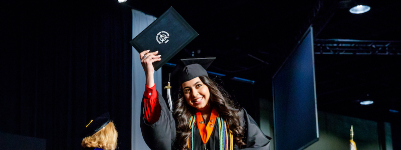 Graduate holding up degree on stage during Commencement ceremony