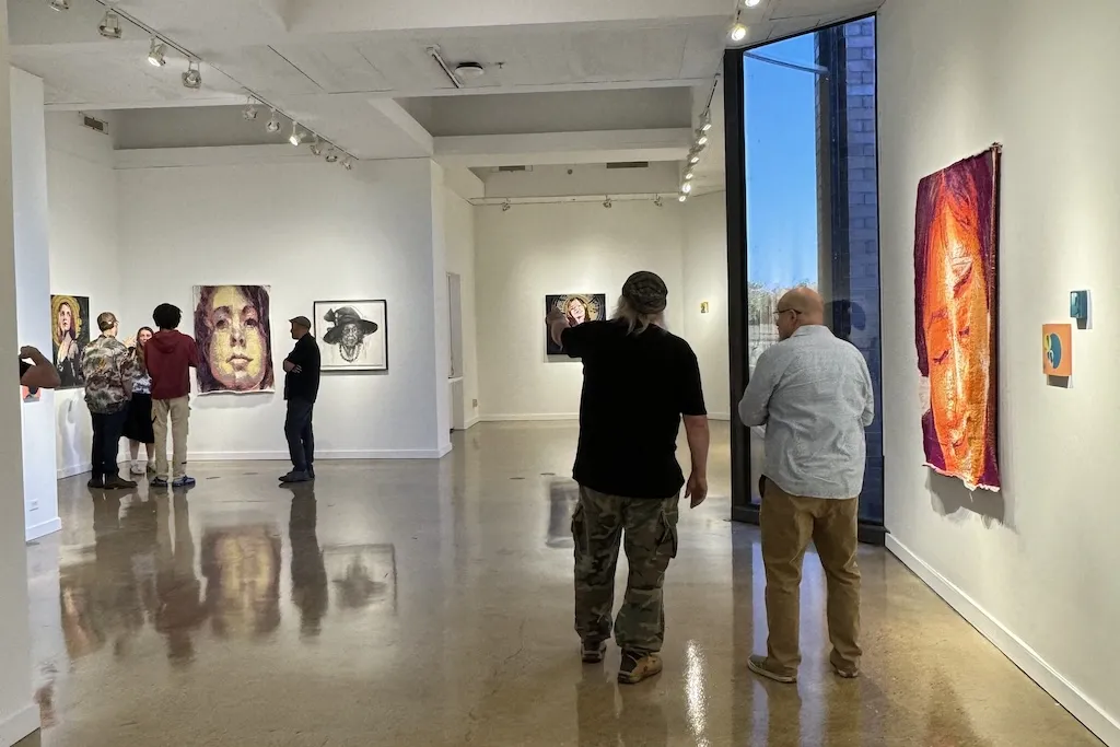 People view colorful paintings in a modern art gallery with bright lights and a large window.