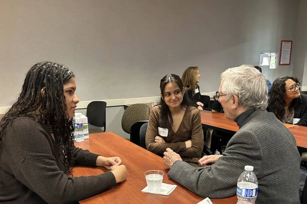 Students talking with Dr. Greer at a table in a classroom.