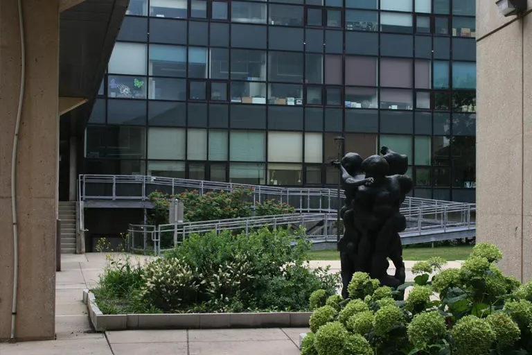 Dark sculpture in a green courtyard with a modern building and dark windows.