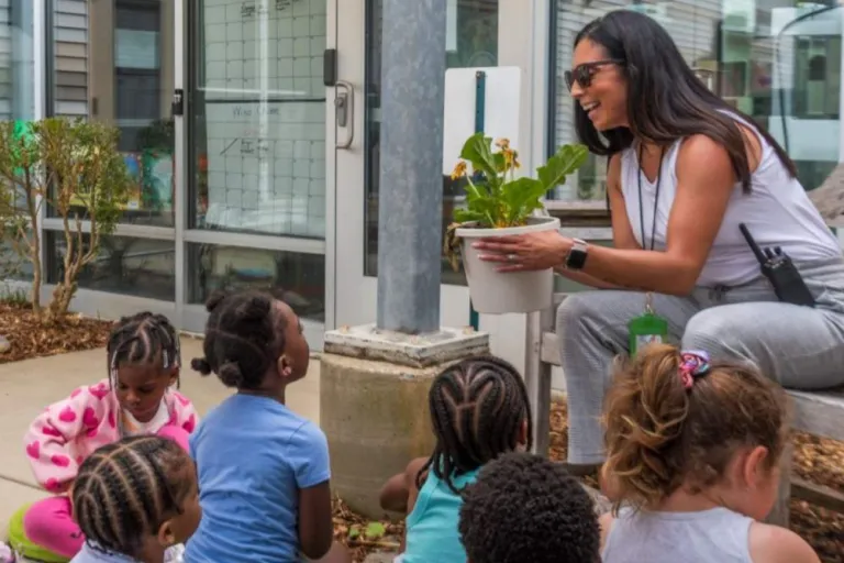 Teacher holding flower pot, with young students gathered around
