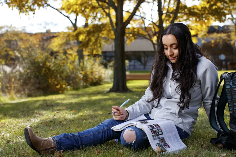 Student sits under tree reading book