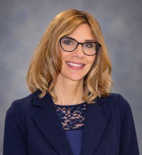 Professional headshot of a smiling woman with glasses and blonde hair.