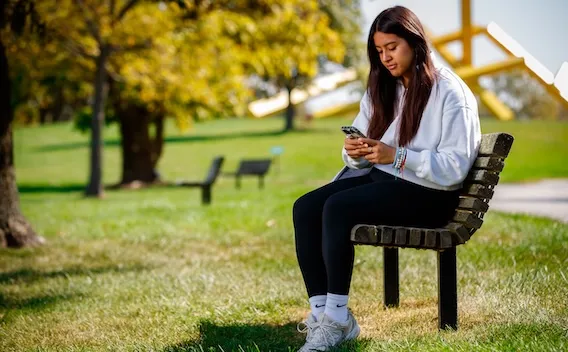 Student sitting on a bench typing on phone