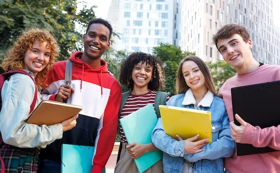 Students standing outdoors, holding books, and smiling