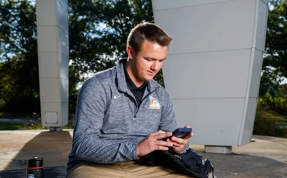 Person sitting outdoors, looking at smartphone.