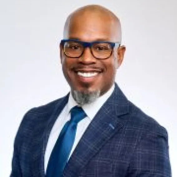 Professional head shot of man in glasses and goatee, wearing blue suit and tie