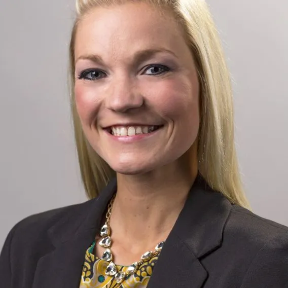 Professional headshot of woman with long blonde hair, wearing dark blazer and patterned blouse.