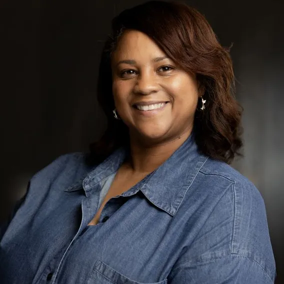 Professional headshot of woman with medium-length brown hair, wearing a denim shirt