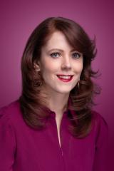 Smiling woman with red hair and red lipstick, wearing a purple shirt.