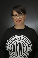 Smiling woman with dark hair and glasses wearing a black DKNY sweatshirt.