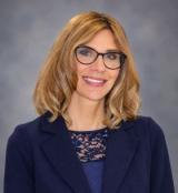 Professional headshot of a smiling woman with glasses and blonde hair.