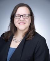 Smiling woman in glasses and a dark professional jacket.