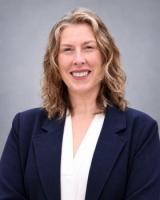 Smiling woman with wavy brown hair, wearing a dark blue blazer.