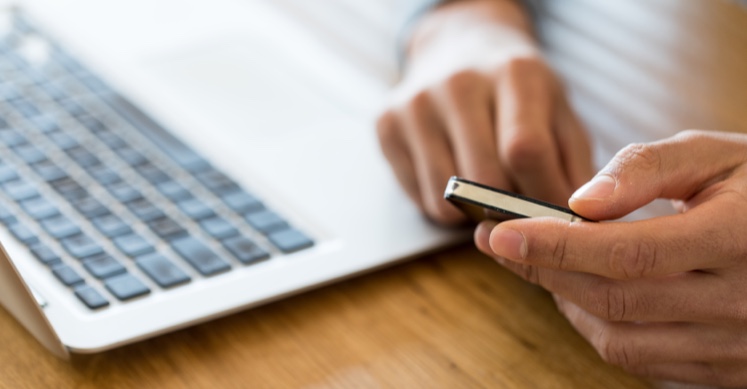 Man holding a phone by a laptop