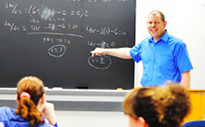 Instructor pointing to math formulas on chalkboard