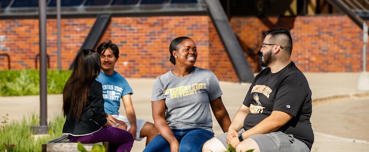 Students talking on bench outside of campus entrance